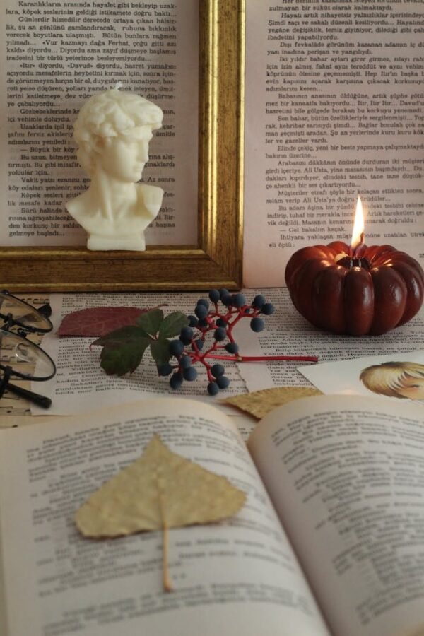 Artistic still life featuring a carved bust, candle, and open book on a decorated table.